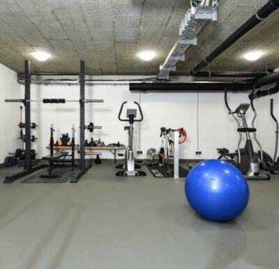 Das Bild zeigt einen Keller mit Sportgeräten wie einer Hantelbank, einem Fahrrad und einem Gymnastikball.